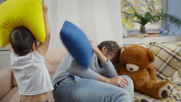 Happy Father and Two Sons Fighting with Pillows Playing Together on Couch