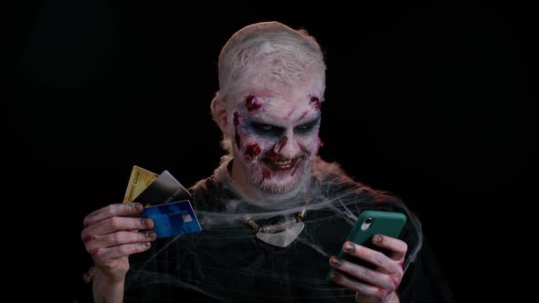 Sinister Man Halloween Zombie Using Credit Bank Cards and Smartphone While Purchases Online Shopping