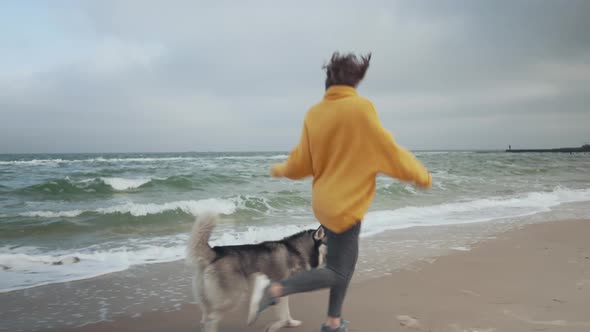 Young Beautiful Female Walking with Siberian Husky Dog on the Beach