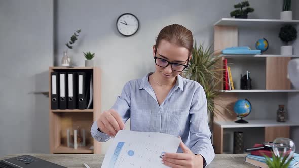 young businesswoman in glasses which sitting in her cabinet and working