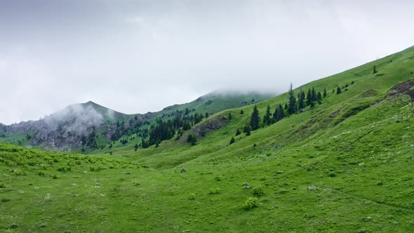 Flying Over Mountain Pass And Lake Among Green Hills On Moody Day