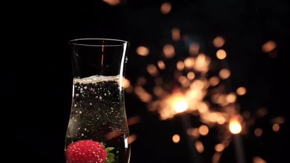 Strawberry splashing on champagne flute with sparklers fireworks on black background. Fruit berry an