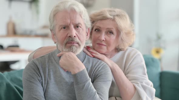 Embracing Old Couple Looking at Camera While Sitting on Sofa