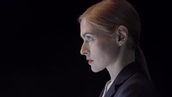 Side profile portrait of a confident young business woman dressed in a suit shot in a studio on a bl