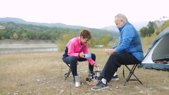 Happy Senior Couple Eating and Drinking While Camping Outdoor in Front of Lake Elderly Travel