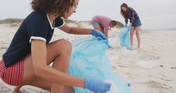 Diverse group of female friends wearing latex gloves collecting rubbish from the beach