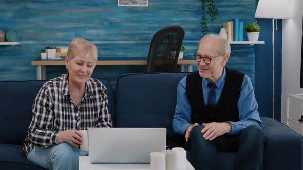 Happy Senior Couple Waving at Videocall with Nephews Using Laptop