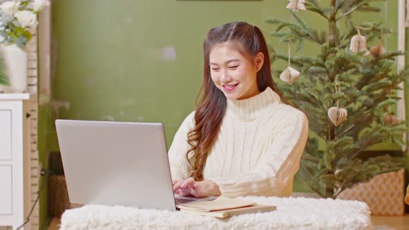 Asian businesswoman working staying at home with christmas tree in background celebrating