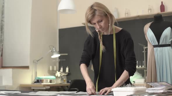 Blonde Caucasian Female in Black Dress with Tailor's Meter Around Neck Pinning Pieces of Fabric