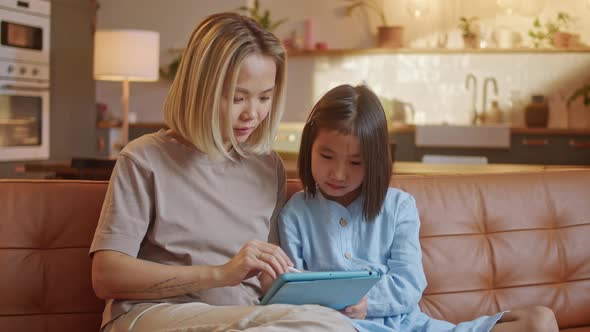 Asian Family and Little Daughter Sit Together on Sofa at Home With Tablet Device Choose Buy Goods on