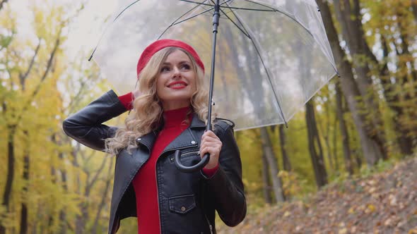 Portrait of a Smiling Happy Cheerful Woman in a Red Suit with a Transparent Umbrella on a Rainy Day