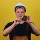 Young Handsome Builder in a Hardhat Holds a Tape Measure Ruler in His Hands on a Yellow Background - VideoHive Item for Sale