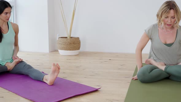 Young Woman in Lotus Position Practicing Yoga with Trainer