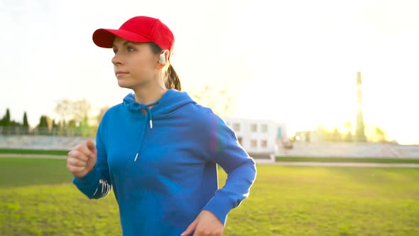 Woman with Wireless Headphones Runs Through the Stadium at Sunset