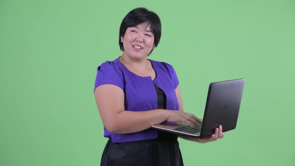 Happy Young Overweight Asian Woman Thinking While Using Laptop