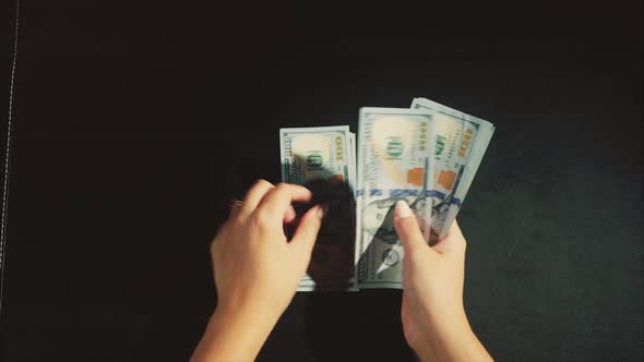 Woman Hands Count a Pack of Dollars on the Black Background