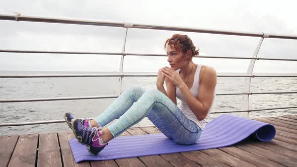Young Athletic Woman Doing Situps on the Mat and Boxing Doing Kicks By the Ocean in the Early