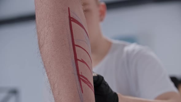 Young Man Drawing a Sketch for Tattoo on the Leg with a Red Marker