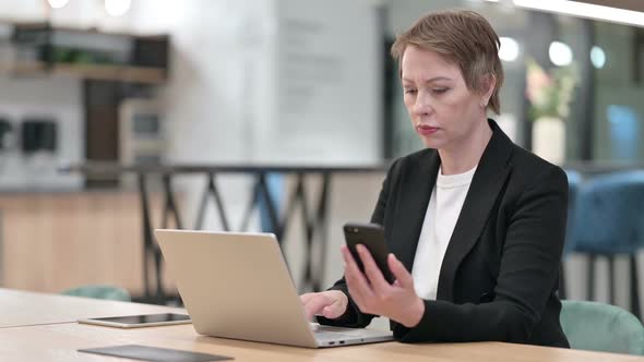 Attractive Old Businesswoman Using Smartphone and Laptop