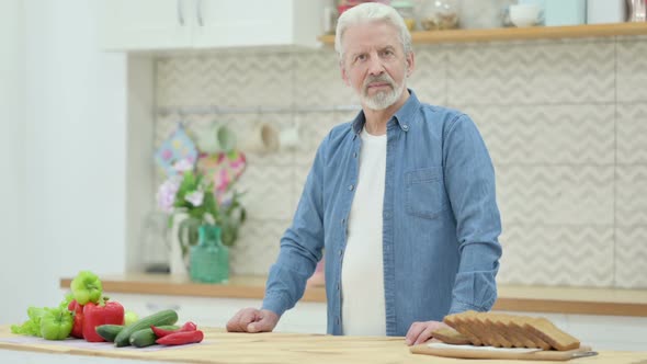 Old Man Looking at the Camera While Standing in Kitchen