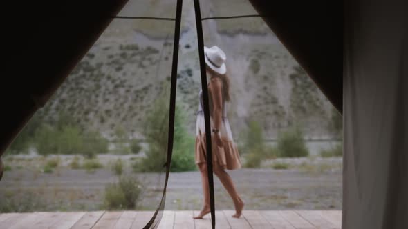 A Girl Traveler in a Light Dress and Hat is Resting in a Tent Casket Walking Along the Terrace and