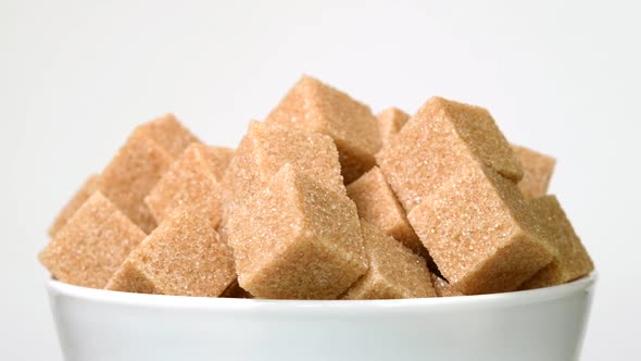 Cubes of Brown Cane Sugar in Bowl Rotating Close-Up on White Background