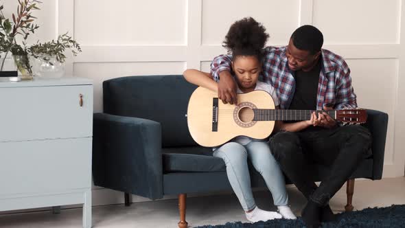 AfricanAmerican Man Teaching His Little Daughter to Play Guitar at Home