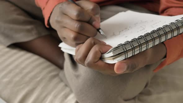 AfricanAmerican Man Writes in Notebook Sitting on Soft Bed