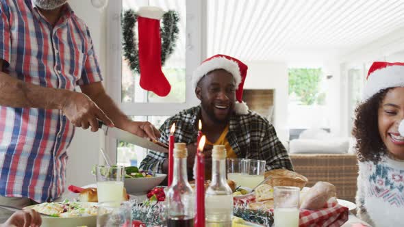 Happy african american multi generation family wearing santa hats and celebrating holiday meal