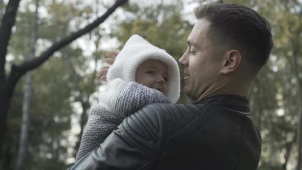 Shooting Over Shoulder of Happy Smiling Man Holding Infant Son and Talking