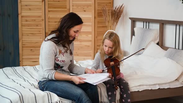 Little Girl Practicing Violin with Mother at Home