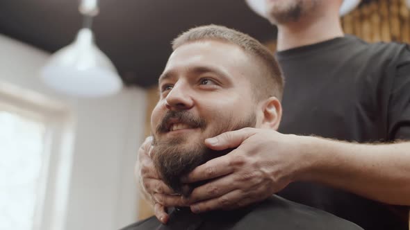 Barber's hands are laying and stroking beard of a Caucasian man, portrait, bottom view.