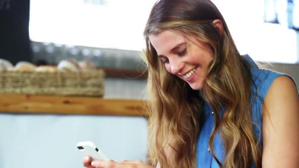 Woman text messaging on mobile phone in cafeteria