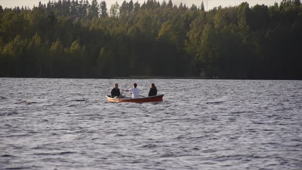 Young adults racing and rowing a boat on a lake at sunset.