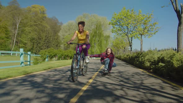 Cheerful Multiracial Females Enjoying Leisure Cycling and Skateboarding Outdoors