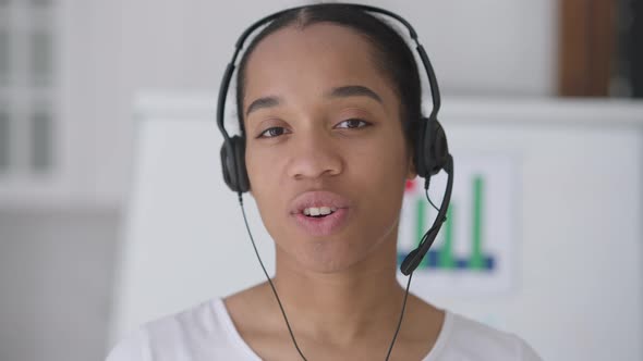 Headshot of Young Slim African American Woman in Earphones Waving and Talking Looking at Camera