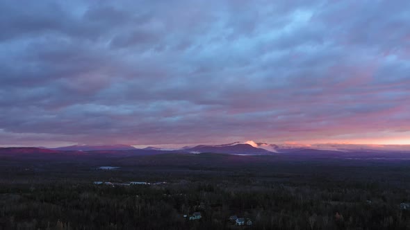 Aerial footage flying backwards at sunrise over a late fall forest with misty mountains in the dista