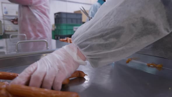 Workers of the Meat Processing Factory Separate Readymade Sausages with Scissors for the Packaging