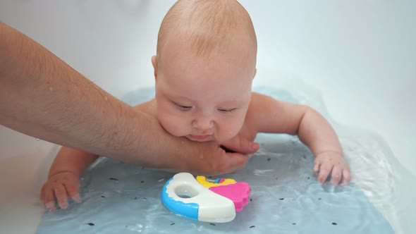 Interested Baby Girl Plays with Father and Toy in Water