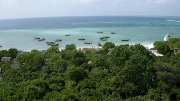 Anchored boats on Zanzibar coast with lush rainforest, drone shot.