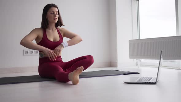 Sporty Woman Doing Stretching Exercise on Yoga Mat While Watching Fitness Video Online on Laptop