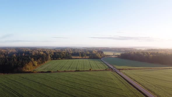 Drone flying over a small country road with green farming fields on the sides. Sideway movement. Lit