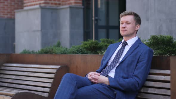 Pensive Businessman Sitting Relax on bench Outside office