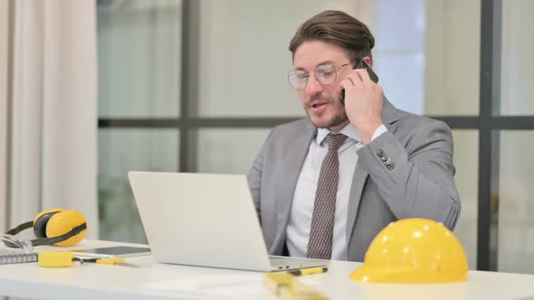 Middle Aged Engineer Talking on Phone while using Laptop in Office