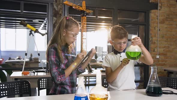 Two Young Scholars of Caucasian Pupils in Safety Goggles Doing Experiment