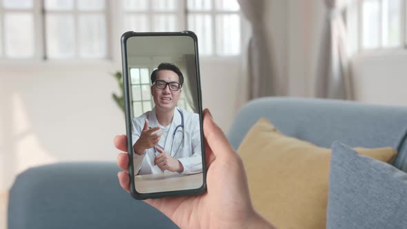 Close-Up Of A Person Video Conferencing With Asian Male Doctor On Smartphone