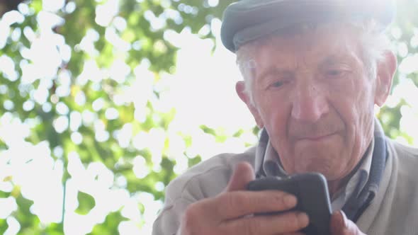 Old Man with a Sad Expression He Holds a Smartphone in His Hands