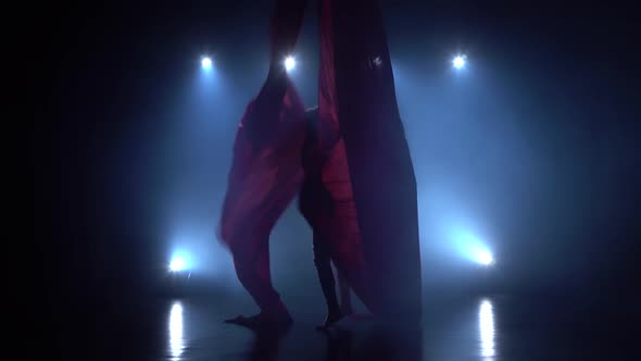 Graceful Gymnast Performing Aerial Exercise with Red Silk on Blue Light Background 083