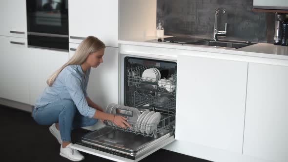 Young Pretty Woman Unloading Dishwasher in Modern Stylish Kitchen