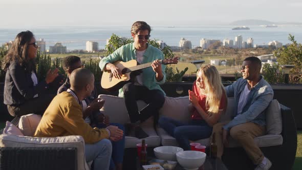 Young Caucasian man playing guitar on a rooftop with his friends